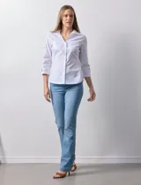 Camisa blanca de algodón con cuello clásico, solapa y escote en V. Tiene mangas tres cuartos con detalle de aberturas cruzadas. Presenta dos bolsillos delanteros aplicados y laterales en tejido modal.