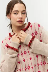 Cárdigan de punto color beige con cuello polo con volados azules, cierre frontal con botones y estampado de corazones y flores en azul y gris.