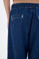 Pantalón jean parachute de denim azul, corte holgado, con cintura y tobillos ajustables con elástico y cordón.