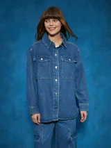 Sobrecamisa de denim azul con cuello camisero, cierre frontal con botones a presión, mangas largas con puños abotonados, dos bolsillos con solapa abotonada en el pecho y corte recto.