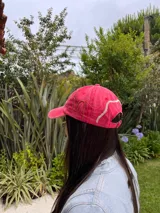 Gorro estilo visera de color rosa desgastado, con bordados artesanales en hilo dorado y blanco que simulan líneas onduladas.