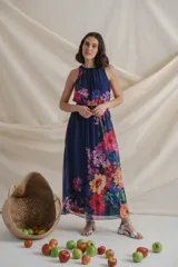 Vestido largo de gasa estampada con flores en tonos lila y rojo sobre fondo azul. Tiene cintura elastizada y cuello halter.