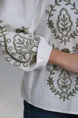 Camisa blanca de manga larga con elástico en puños, cuello mao con botones en la parte delantera y bordados florales en verde.