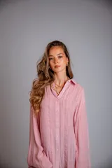 Camisa color beige claro, de corte holgado, con cuello clásico, cierre frontal con botones, mangas largas con puños abotonados y detalles de broderie en la parte delantera.