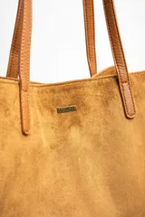 Bolso tipo tote bag grande color camel, confeccionado en cuero vegano con textura de gamuza. Tiene doble asa de hombro y logo de la marca en el frente.
