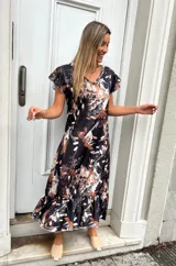 Vestido midi negro con estampado abstracto en tonos beige y blanco, mangas cortas con volados y falda con volados en el ruedo.