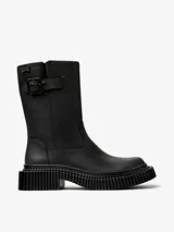 Bota de media caña color negro, con diseño de suela gruesa y estriada. Presenta una correa con hebilla en la parte superior de la caña y un logo de la marca "Camper" en una etiqueta.