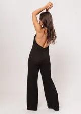 Mono largo negro de punto con escote halter y corte palazzo. Incluye un collar largo con dijes de estrellas plateadas.