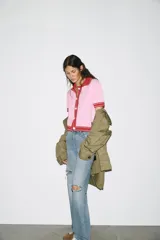 Chaqueta color blanco de punto con cuello solapa y manga corta. Tiene cierre frontal con botones color naranja y ribete en azul marino y naranja.