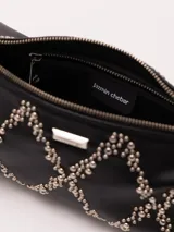 Mini cartera de cuero vacuno negro, decorada con tachitas metálicas y lingote. Cuenta con correa corta y cierre metálico.