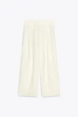 Pantalón culotte color crudo, de tiro medio, confeccionado en lino. Presenta bolsillos laterales, pinzas delanteras, pierna ancha y cierre frontal con cremallera, botón y ganchos metálicos.