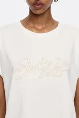 Camiseta blanca de algodón con corte recto, cuello redondo y mangas cortas tipo murciélago. Estampado frontal con el logo de la marca Bimba y Lola en color beige.