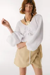 Top blanco de lino italiano con escote en V, mangas largas estilo globo y jareta ajustable en la parte delantera que crea un efecto fruncido y volado en el ruedo.