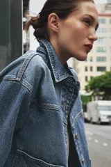 Cazadora de denim celeste de corte recto, con cuello solapa, manga larga, bolsillos delanteros de plastrón y cierre frontal con botones metálicos.