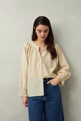 Camisa color crema de lino con cuello redondo, canesú fruncido, mangas largas amplias con puños elastizados con volado y cierre frontal con botones.
