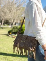 Mini bandolera de cuero con estampado de piel de serpiente en tonos blanco y negro, con flecos largos y hebilla metálica.