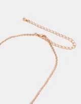 Collar corto bañado en oro rosa con cadena de eslabones y tres dijes de moño con strass rosado.