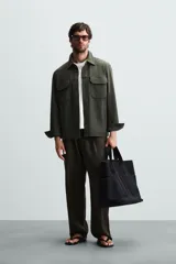 Sobrecamisa color beige de corte relaxed fit, confeccionada en tejido con elasticidad. Tiene cuello solapa, manga larga con puños abotonados, bolsillos de parche con solapa en el pecho y bolsillos de ojal en la cadera. El cierre es frontal con botones.