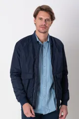 Campera bomber verde militar de nylon, con cuello, puños y ruedo acanalados. Tiene bolsillos laterales con solapa y botón.