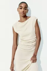 Vestido midi color crema, de punto arrugado, con mangas japonesas, escote barco y laterales fruncidos que crean un efecto drapeado.