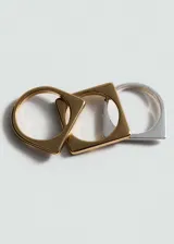 Set de tres anillos de metal con diseño geométrico: uno dorado con forma cuadrada, uno plateado con forma circular y uno plateado con forma cuadrada.
