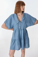Vestido corto celeste de lino, con cuello tipo polo con detalle de puntilla, mangas cortas y falda escalonada con volantes.