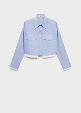 Camisa celeste de popelina de algodón con diseño crop, cuello camisero, cierre frontal con botones, dos bolsillos de solapa en la parte delantera, manga larga con puños abotonados y terminaciones en contraste blanco.