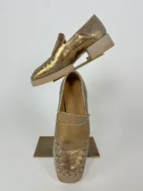 Mocasines dorados de cuero con suela beige.