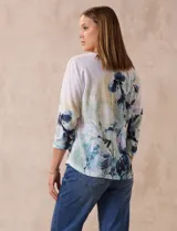 Buzo blanco estampado con flores azules y detalles en verde y amarillo, de la marca Milano. Tiene cuello redondo y mangas 3/4 con apliques de brillos en el frente.