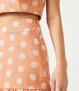 Conjunto de pollera corta y top color salmón con estampado de flores blancas. El top es corto con tirantes finos y la pollera tiene volados en el ruedo.