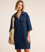Vestido corto de jean azul con cuello camisero, escote en V, mangas cortas, dos bolsillos delanteros y corte recto.