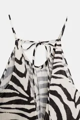 Mono largo de mujer con estampado de cebra en blanco y negro. Presenta un diseño de cuello halter con tirantes finos que se atan en la nuca, escote redondo y pierna ancha con bajo ajustable mediante lazadas.
