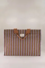 Bolso tote de algodón a rayas verticales marrones, azules y rojas, con asas de mano marrones. Tiene un bolsillo lateral interior grande, un bolsillo para el teléfono y un bolsillo para las llaves.