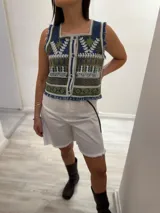 Chaleco corto de denim azul con bordado artesanal en tonos naranja, blanco y marrón. Tiene escote cuadrado, cierre de botones y terminaciones desflecadas.