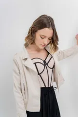 Chaqueta color beige de tela tipo gamuza con elastano, cuello solapa, manga larga con trabillas en hombro, bolsillos delanteros con cremallera metálica y cierre frontal con cremallera.