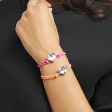 Pulsera de hilo elástico doble color rosa vibrante, con un dije central de corazón plateado de apariencia tridimensional y un cierre de bola metálica plateada.
