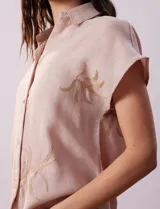 Camisa color beige con estampado de hojas marrones, de manga corta, con cuello a la base con solapa y escote en V.