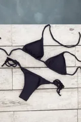 Conjunto de bikini negro con corpiño de triángulos movibles con tiras para atar al cuello y espalda, y bombacha colaless con tiras para atar a los costados.