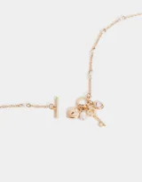 Collar de cadena corta dorada con dijes estilo vintage: corazón, llave, perla y cristal.