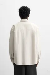 Camisa color crema de corte relaxed fit, confeccionada en tejido de mezcla de algodón suave al tacto. Tiene cuello solapa, manga larga con puños abotonados, un bolsillo de parche en el pecho y cierre frontal con botones.