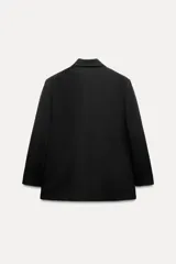 Blazer negra oversize con cuello solapa, manga larga con hombreras, bolsillos delanteros con solapa y cierre frontal cruzado con botones.