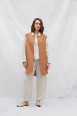 Camisa larga de lino color beige, con cuello camisero y cierre frontal con botones. Tiene mangas largas con puños abotonados, bolsillos laterales y una franja a contratono en la espalda y mangas.