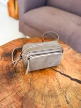 Bandolera color visón, fabricada en cuero con forro de tela. Tiene bolsillo interior y exterior. Entra billetera grande.