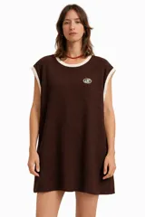 Vestido corto de tejido de punto marrón oscuro, sin mangas, con cuello redondo ribeteado en color crema y un pequeño logo bordado en el pecho.