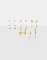 Set de seis pares de aros dorados con distintos diseños: aros colgantes con argollas y dijes de corazón, aros largos con perlas y dijes de metal, aros con forma de campana y aros con forma de moño.
