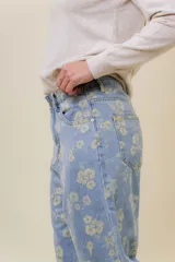 Pantalón de jean de tiro medio-alto, pierna ancha y lavado celeste claro, con estampado floral en tono amarillo pálido.