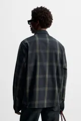 Camisa de hombre regular fit confeccionada en tejido de algodón a cuadros en tonos azul oscuro y verde oliva. Tiene cuello solapa, manga larga con puños abotonados, bolsillo de plastrón en el pecho y cierre frontal con botones.