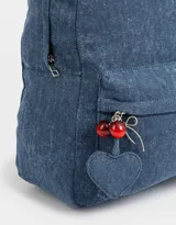 Mochila azul de denim con bolsillo frontal con cierre y tirador con charms decorativos. Tiene correas regulables, manija superior y cierre superior.