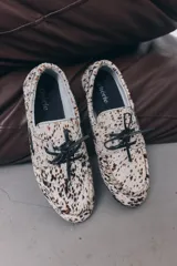 Mocasines con capellada de cuero con estampado animal print en tonos blanco y marrón. Presentan cordones de cuero negro y suela plana.