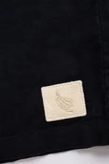 Camisa negra de manga corta con cuello camp y calce relajado. Confeccionada en mezcla de algodón y lino con botones de coco con logo y parche característico de Polonio.